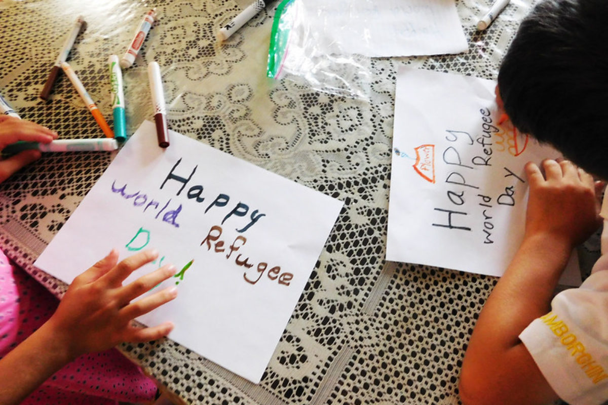 Photo showing two resettled children in the U.S. drawing illustrations for World Refugee Day